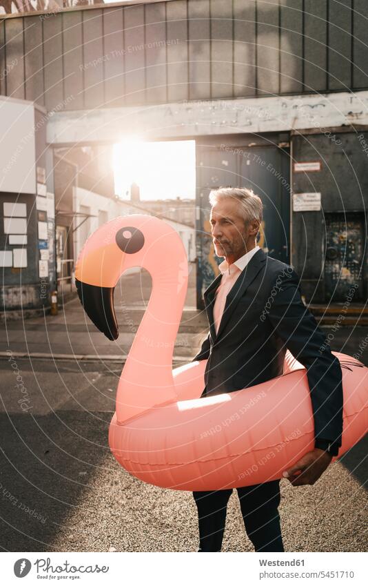 Mature businessman on the street with inflatable flamingo Businessman Business man Businessmen Business men business people businesspeople business world