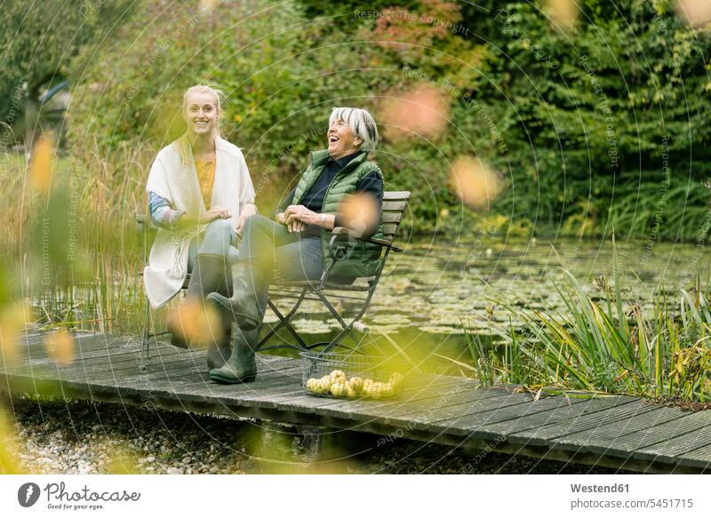 Happy young woman with her grandmother sitting on jetty at garden pond Pond Ponds grandmas grandmothers granny grannies boardwalk boardwalks happiness happy