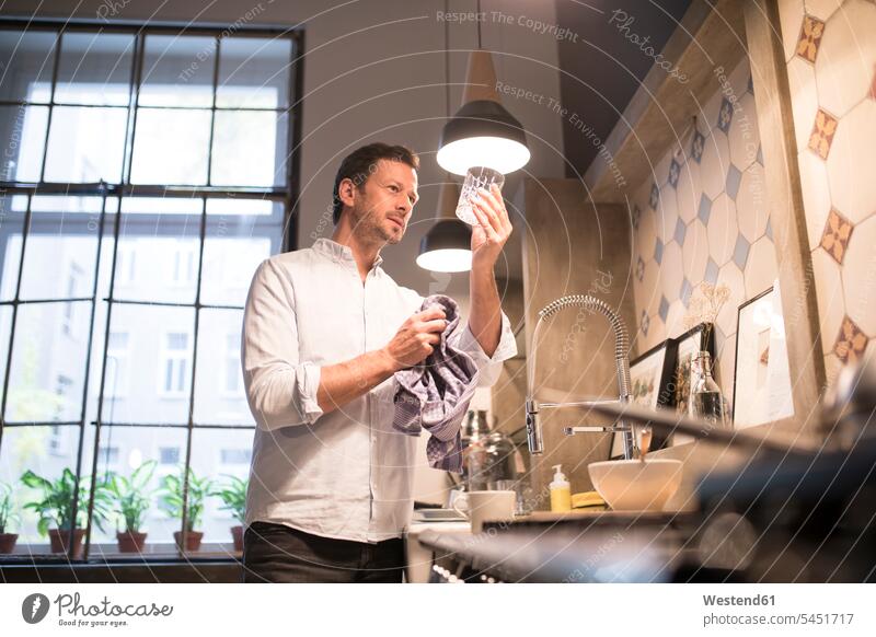 Man in kitchen drying glass with towel man men males domestic kitchen kitchens Adults grown-ups grownups adult people persons human being humans human beings