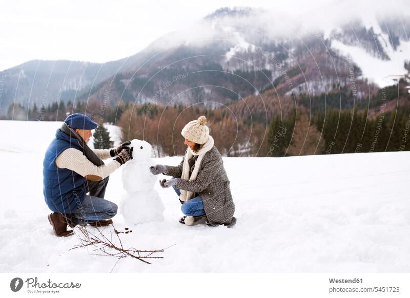 Senior couple building up snowman in winter landscape snowmen twosomes partnership couples people persons human being humans human beings snow-covered