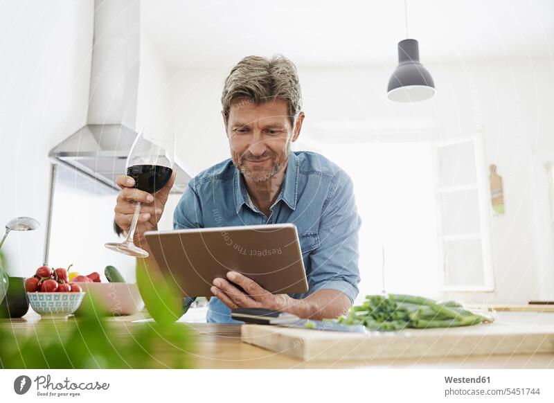 Mature man in his kitchen reading recipe on his digital tablet smiling smile Red Wine Red Wines confidence confident digitizer Tablet Computer Tablet PC