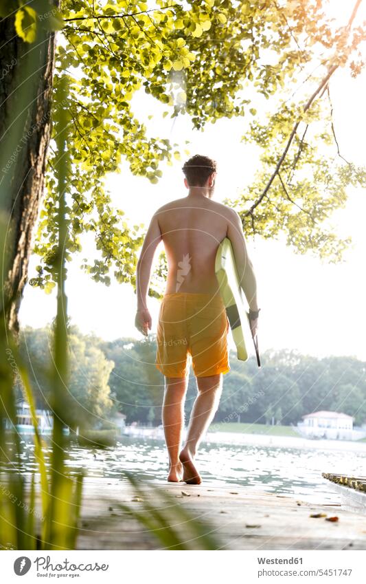 Young man with surfboard walking on a jetty at a lake jetties lakes going surfboards men males water waters body of water surfing surf ride surf riding