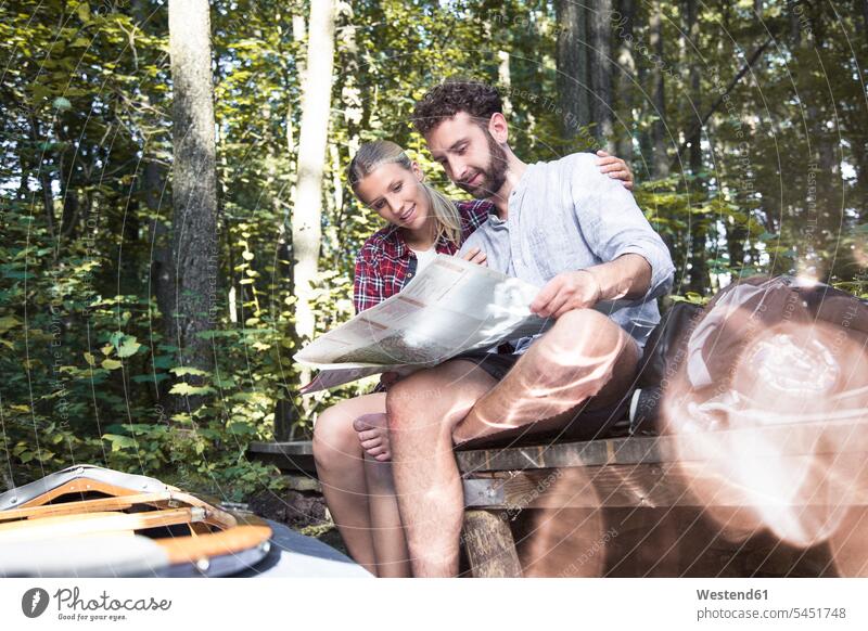 Young couple with map and canoe sitting on a jetty at a forest brook woods forests jetties twosomes partnership couples brooks rivulet Seated maps people