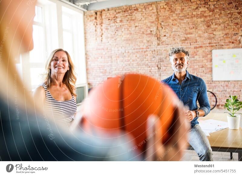 Smiling colleagues with basketball in office Basketball smiling smile offices office room office rooms sport sports workplace work place place of work modern
