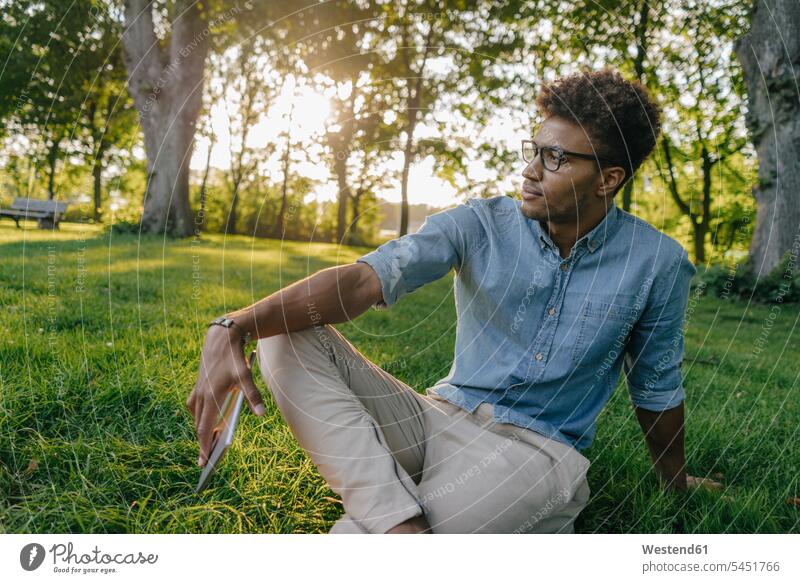 Young man sitting with mobile device in park looking around mobile phone mobiles mobile phones Cellphone cell phone cell phones parks looking round look round