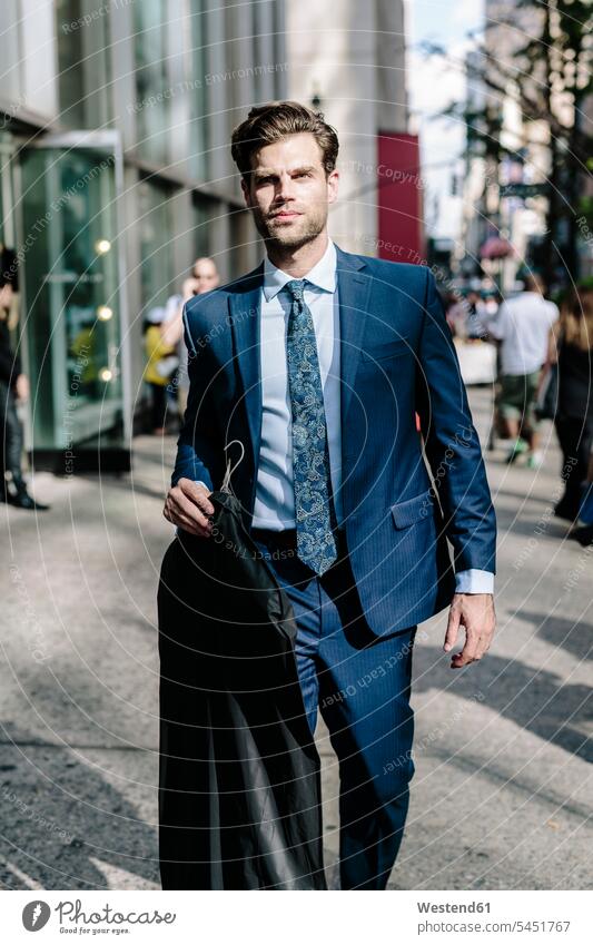 Handsome businessman walking in Manhattan, carrying jacket on a hanger coat coats jackets going Businessman Business man Businessmen Business men suit Fullsuit