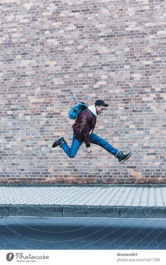 Young man jumping in front of brick wall men males Leaping Adults grown-ups grownups adult people persons human being humans human beings jumps pavement