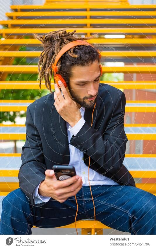 Young businessman with dreadlocks sitting on stairs listening music with headphones and cell phone headset Businessman Business man Businessmen Business men