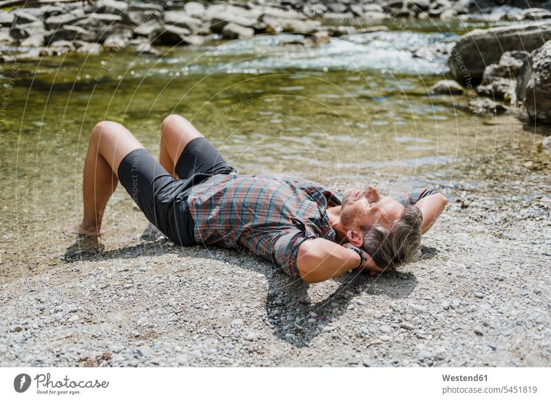 Hiker having a break at the riverbank hiking hike River Rivers water man men males lying laying down lie lying down waters body of water Adults grown-ups