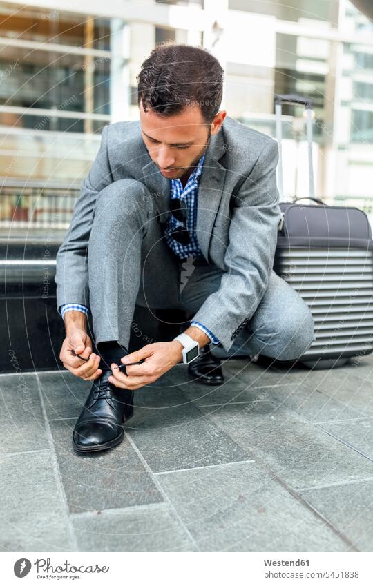 Businessman tying his shoes in the city Business man Businessmen Business men tie suitcase suitcases business people businesspeople business world business life