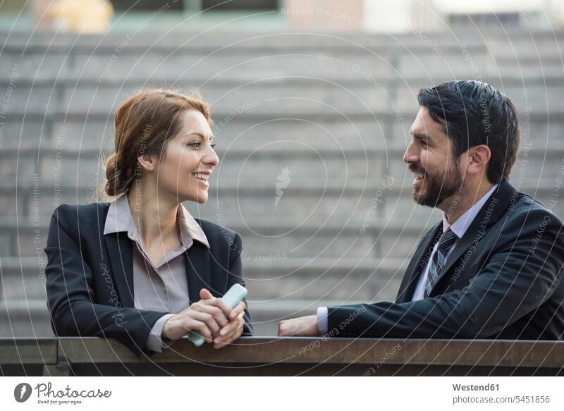 Businesswoman and businessman talking outdoors smiling smile speaking colleagues business world business life men males businesswoman businesswomen
