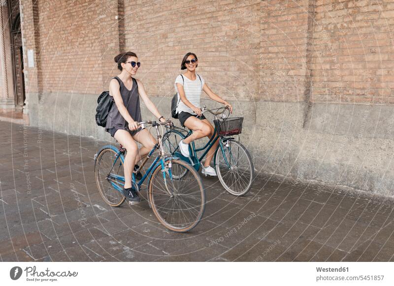 Two young women riding bicycle in the city female friends riding bike bike riding cycling bicycling pedaling mate friendship bikes bicycles cyclist