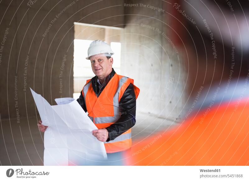Man with plan wearing safety vest in building under construction man men males architect architects construction site Building Site sites Building Sites