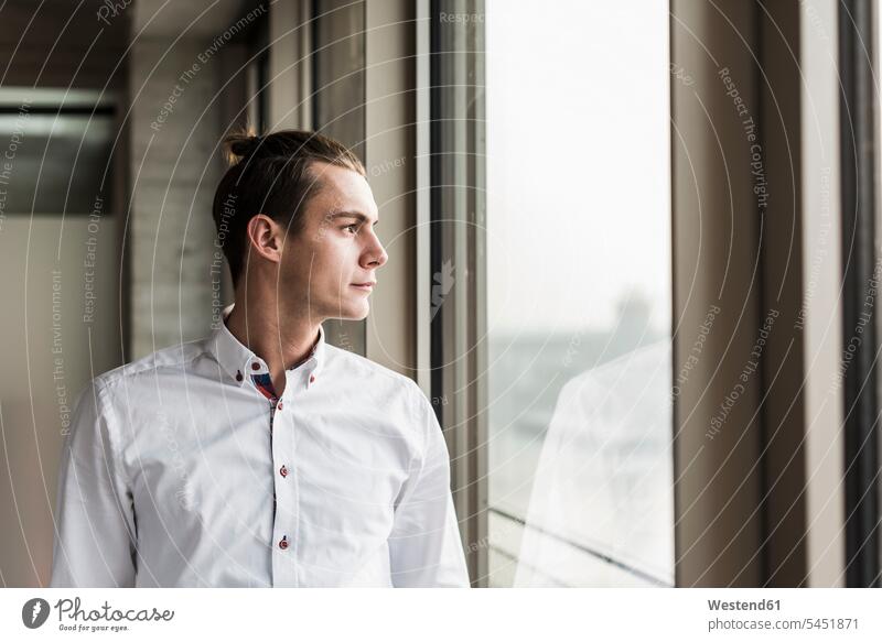 Young businessman looking out of window view seeing viewing windows Businessman Business man Businessmen Business men business people businesspeople