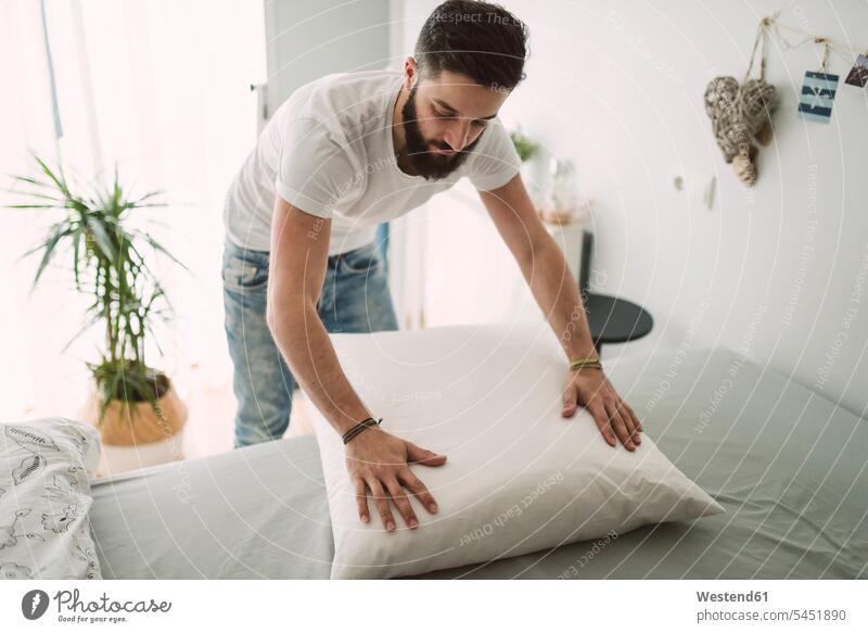Young man making the bed at home beds men males Adults grown-ups grownups adult people persons human being humans human beings caucasian caucasian ethnicity