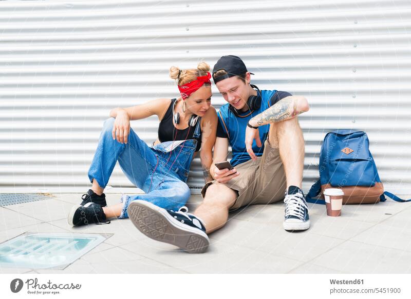 Young couple sitting on ground looking at smartphone twosomes partnership couples Smartphone iPhone Smartphones people persons human being humans human beings