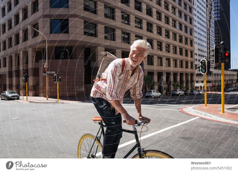 Mature man riding bicycle in the city town cities towns riding bike bike riding cycling bicycling pedaling on the move on the way on the go on the road smiling