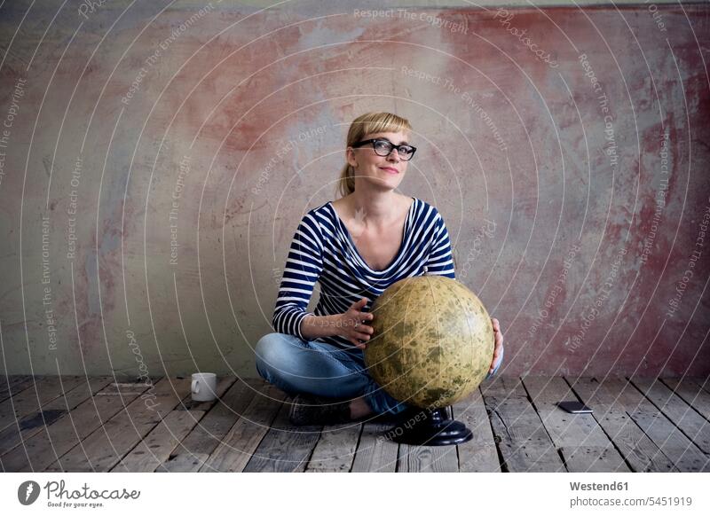Smiling woman sitting on wooden floor in an unrenovated room with an old globe females women portrait portraits globes Adults grown-ups grownups adult people