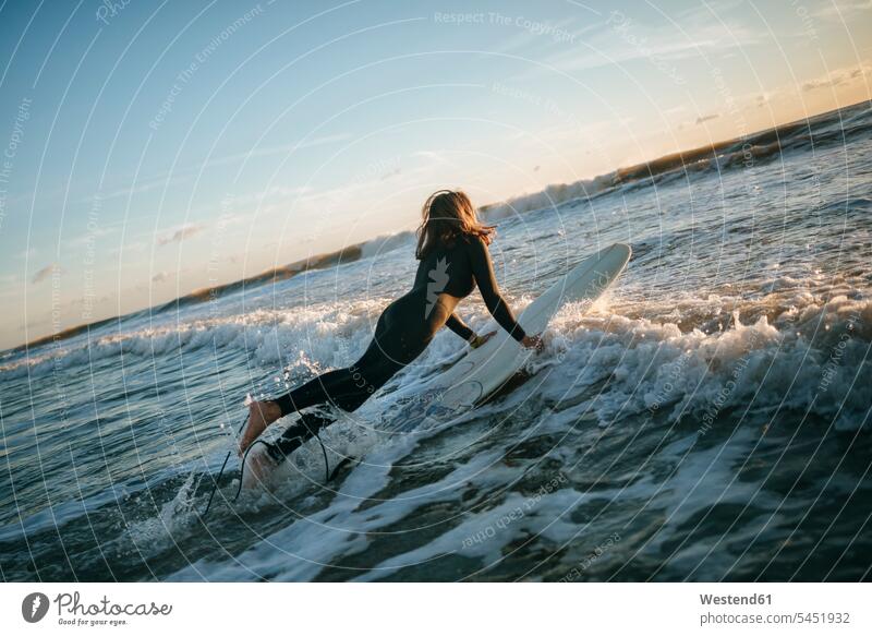 Surfer woman dressed in wetsuit entering the sea with surfboard surfboards surfer female surfer surfers female surfers ocean surfing surf ride surf riding