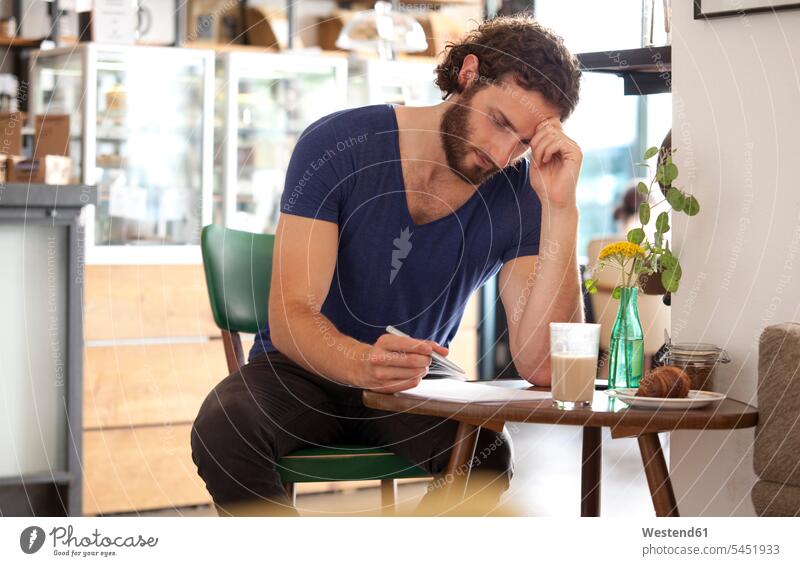 Pensive young man sitting in a coffee shop writing letter write cafe men males Adults grown-ups grownups adult people persons human being humans human beings