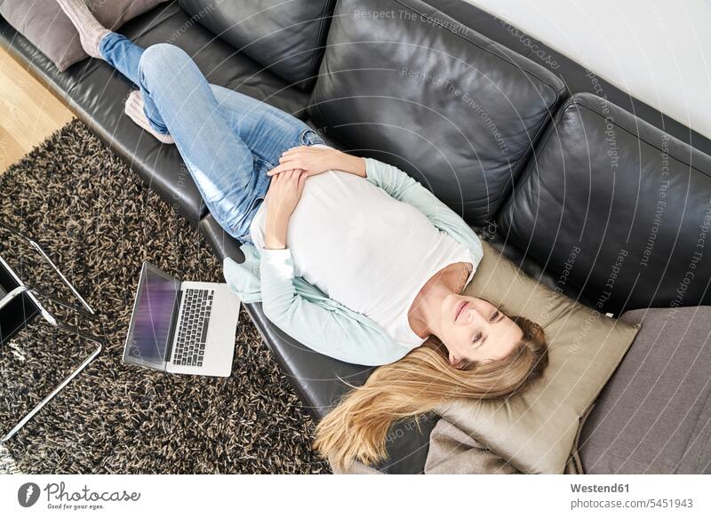 Woman at home lying on couch next to laptop woman females women laying down lie lying down Laptop Computers laptops notebook settee sofa sofas couches settees