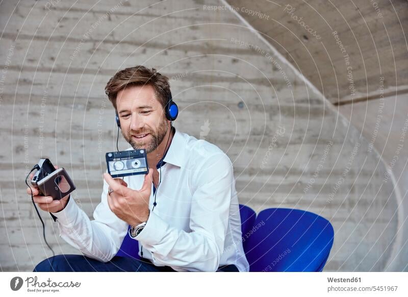 Man sitting on chair listening to music from walkman Businessman Business man Businessmen Business men Seated smiling smile hearing cassette cassettes