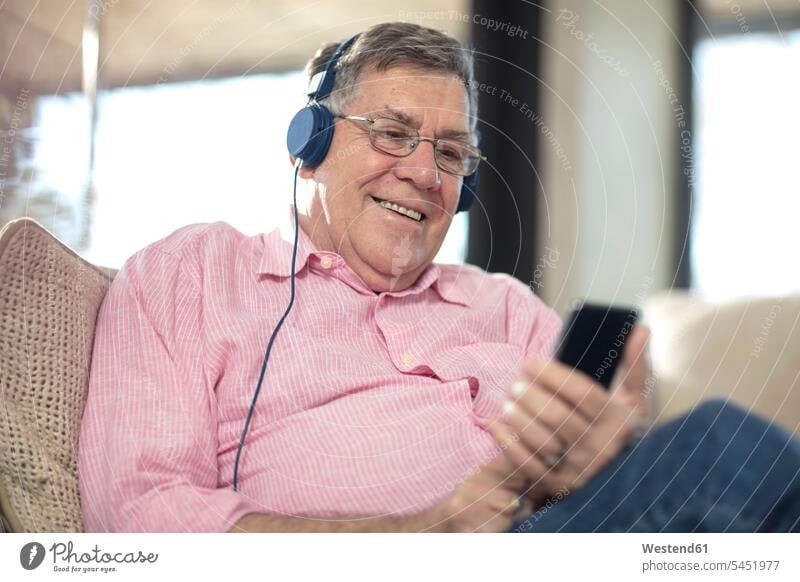 Smiling senior man wearing headphones listening to music at home headset couch settee sofa sofas couches settees hearing men males smiling smile senior men