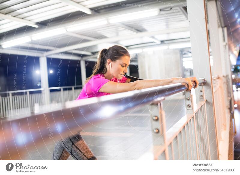 Young woman in pink sportshirt stretching in modern metro station at night Listening Music young women young woman exercising exercise training practising