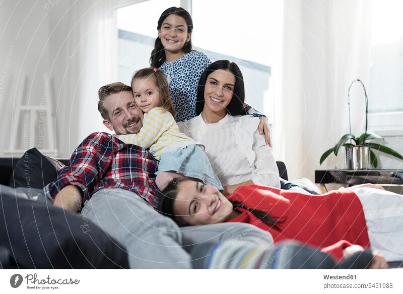 Portrait of parents and three daughers on sofa in living room couch settee sofas couches settees family families smiling smile daughter daughters people persons