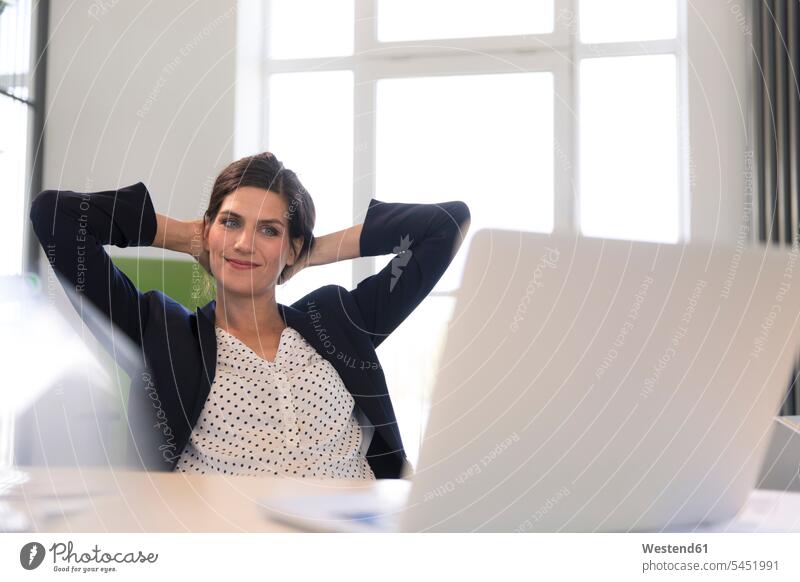 Happy businesswoman sitting in office, looking at laptop with hands behind head smiling smile happiness happy Laptop Computers laptops notebook