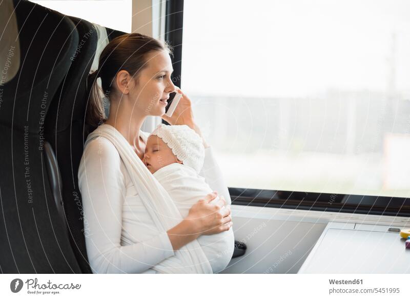 Mother with baby girl traveling by train talking on cell phone on the phone call telephoning On The Telephone calling mobile phone mobiles mobile phones