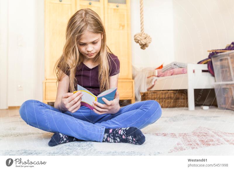 Girl sitting on the floor of children's room reading a book girl females girls books kid kids people persons human being humans human beings Seated Floor Floors