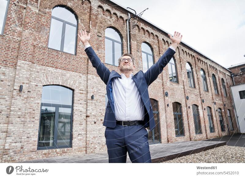 Businessman standing in front of building with arms raised entrepreneur entrepreneurs enterpriser Business man Businessmen Business men business business world