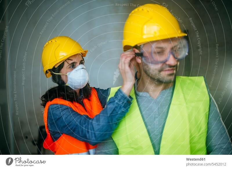 Woman helping man putting on safety glasses on a construction site colleagues working At Work construction worker builders Building Site sites Building Sites