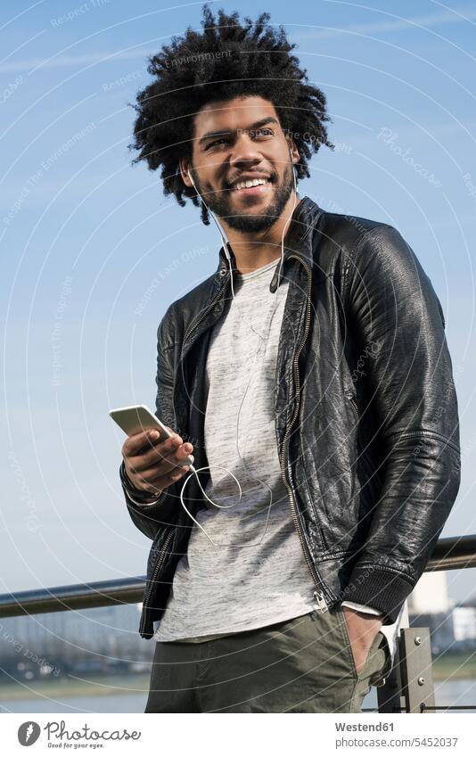Smiling man with earphones listening to music on his smartphone smiling smile men males mobile phone mobiles mobile phones Cellphone cell phone cell phones