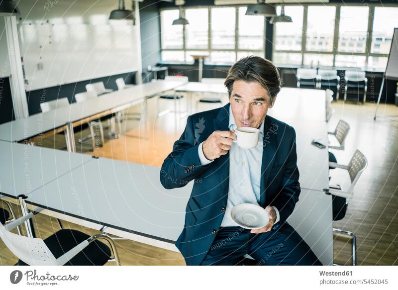 Businessman with cup of coffee sitting on table in meeting room of an office Coffee Table Tables offices office room office rooms Seated Business man