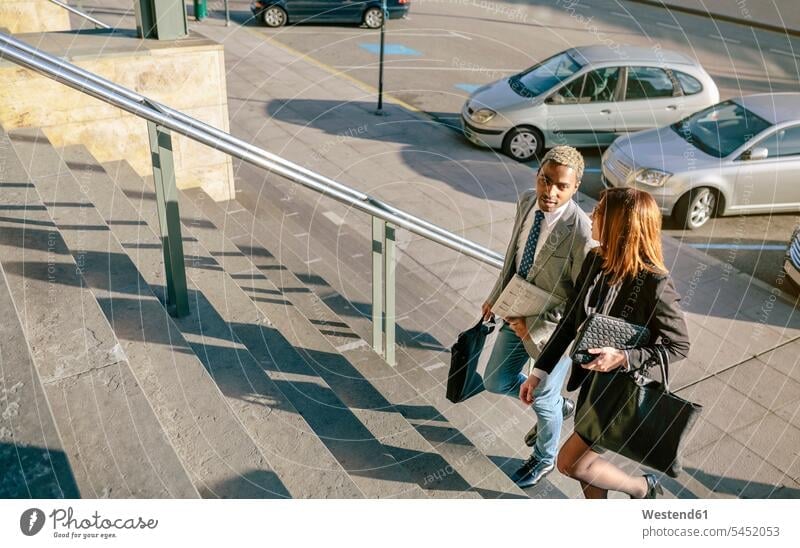Young businessman and woman climbing stairs on the move on the way on the go on the road business people businesspeople talking speaking walking going commuter