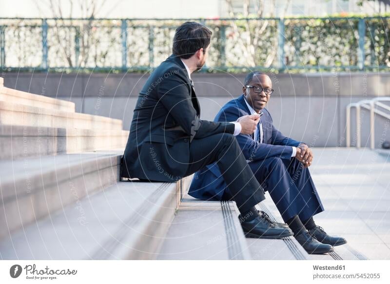Two businessmen sitting on stairs talking Businessman Business man Businessmen Business men stairway colleagues speaking business people businesspeople