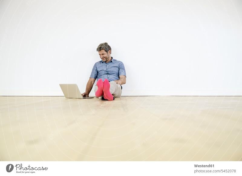 Mature man sitting on ground in empty room, using laptop men males Sitting On The Floor Sitting On Floor home at home Seated working At Work Laptop Computers