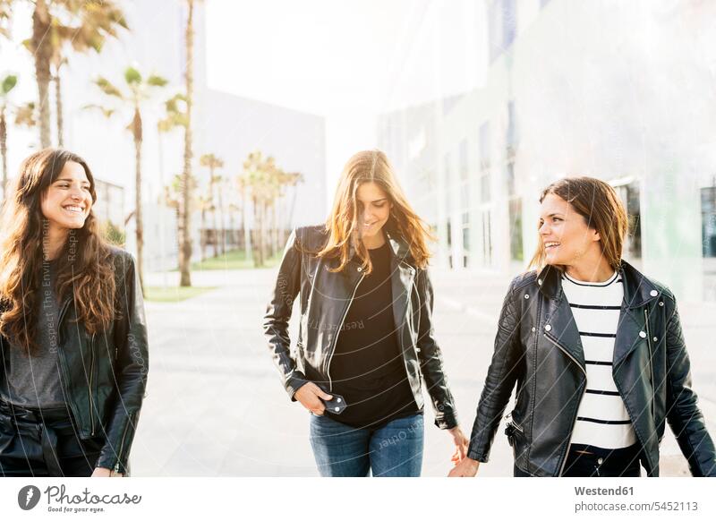 Three happy friends wearing black leather jackets female friends mate friendship laughing Laughter fashion fashionable woman females women walking going