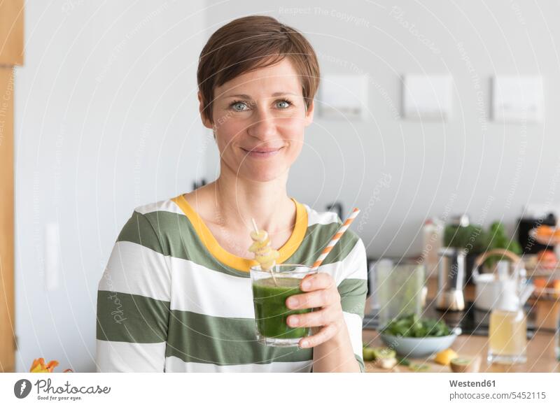Portrait of smiling woman with green smoothie in the kitchen portrait portraits females women Smoothies Adults grown-ups grownups adult people persons