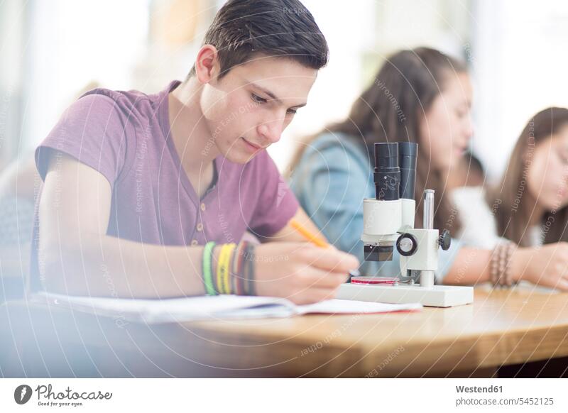 Science student working in class with microscope writing write microscopes learning pupils education school schools caucasian caucasian ethnicity