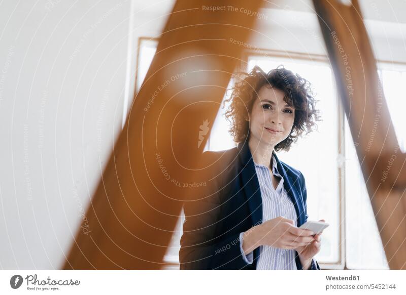 Businesswoman standing by ladder in office, holding smartphone calculating calculate figure out figuring mobile phone mobiles mobile phones Cellphone cell phone