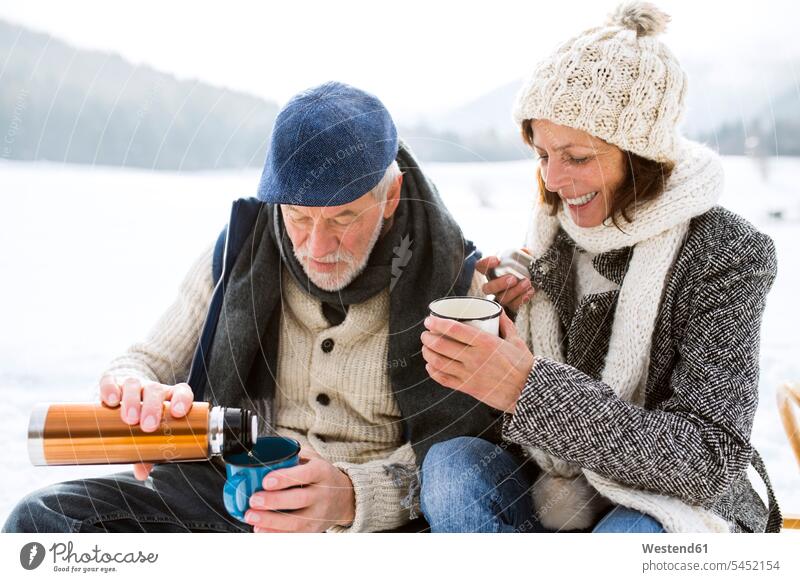 Senior couple having a break with hot beverages in snow-covered winter landscape senior couple elder couples senior couples adult couple adult couples twosomes