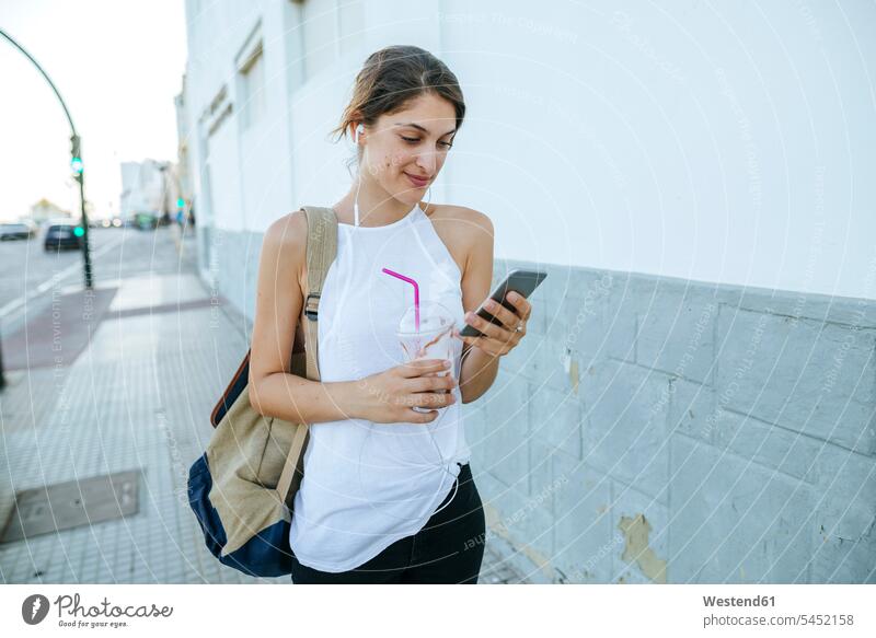 Young woman with cell phone and smoothie walking down the street Smoothies female tourist females women mobile phone mobiles mobile phones Cellphone cell phones