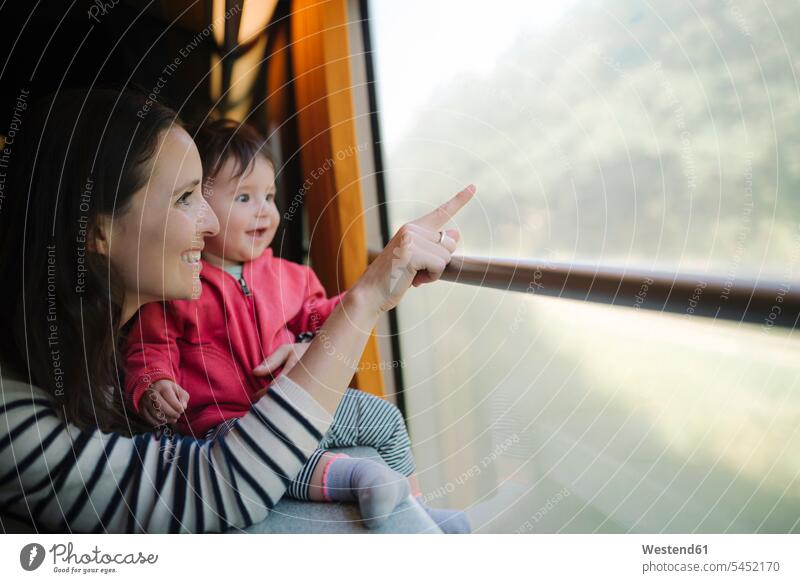 Happy mother and baby girl traveling by train looking out of window windows infants nurselings babies pointing point at pointing at show showing travelling
