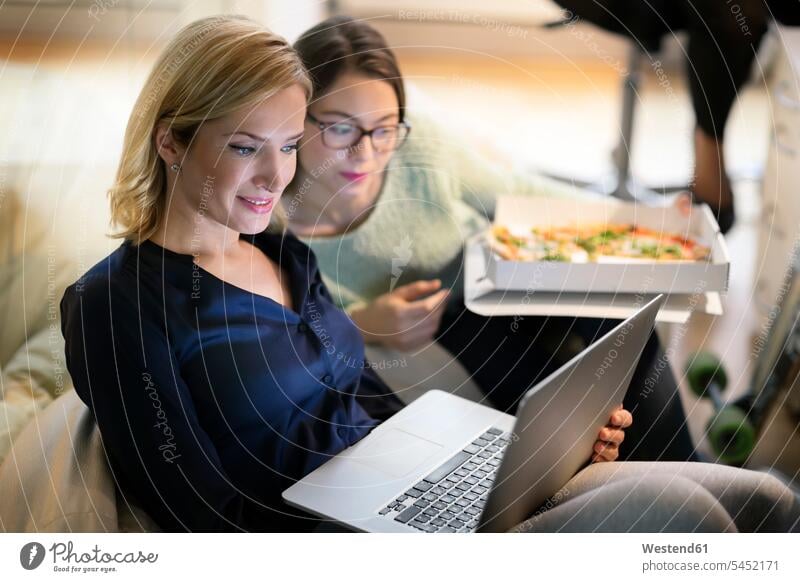 Two businesswomen in office with pizza and laptop Pizza Pizzas businesswoman business woman business women offices office room office rooms Female Colleague