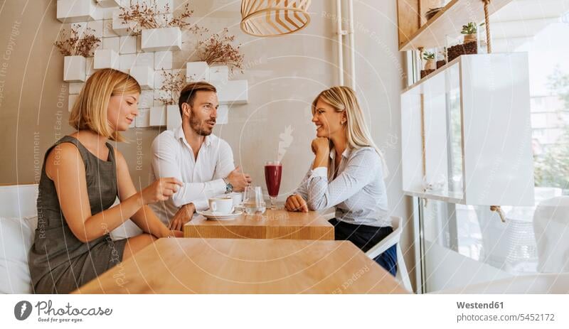 Three friends meeting in a cafe talking speaking smiling smile friendship relaxation relaxed relaxing lifestyle life styles Coffee Cup Coffee Cups confidence