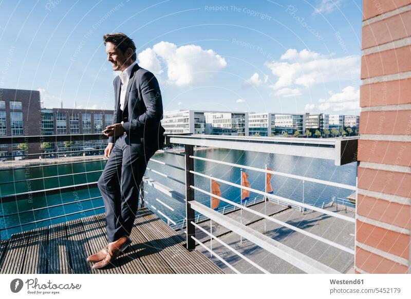 Businessman standing on balcony, holding smartphone Business man Businessmen Business men independence independent balconies smiling smile business people
