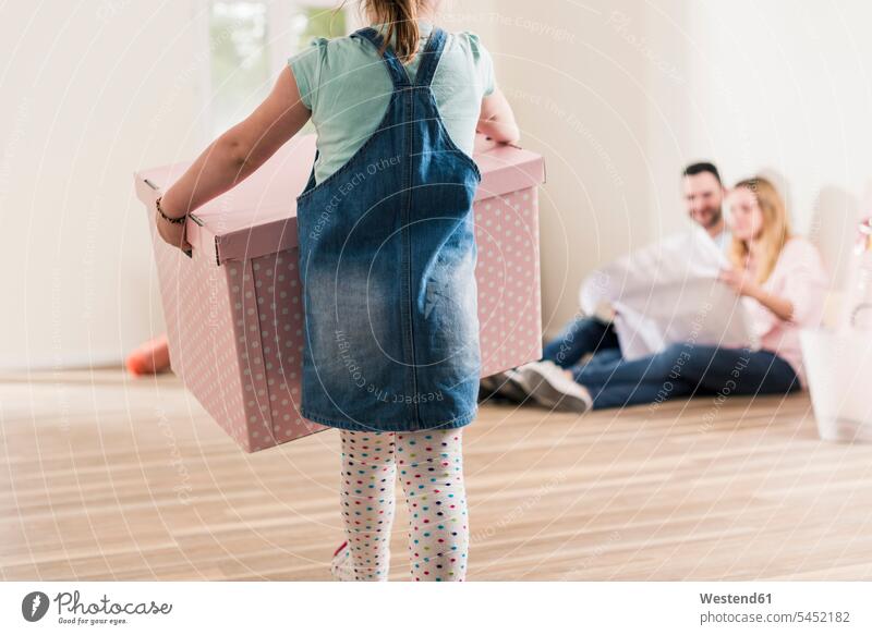 Girl carrying cardboard box in empty apartment with parents in background flat flats apartments Cardboard Carton carton cardboard boxes Cardboards cartons girl